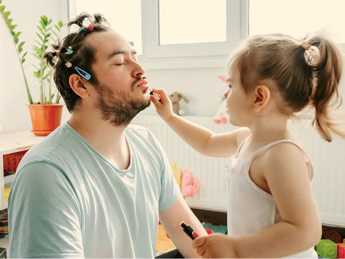 @lang('Pai a sorrir enquanto a filha pequena lhe aplica maquilhagem no rosto, num momento divertido de cumplicidade em casa')